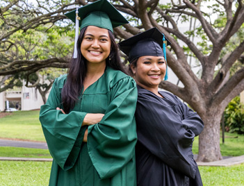 2 female graduating students standing back to back in their cap and gowns